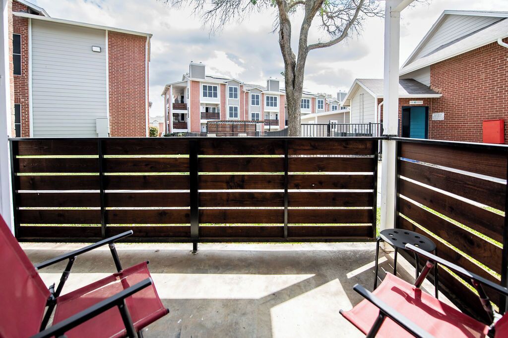 A gated outdoor area with a wooden fence, red chairs, and a view of apartment buildings in the background.