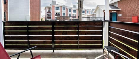 A gated outdoor area with a wooden fence, red chairs, and a view of apartment buildings in the background.