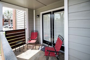 A covered porch with two red chairs and a small table, a brick column, and a view of a street with parked cars.