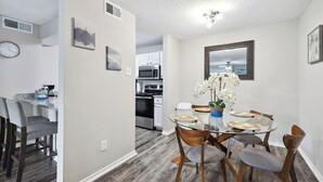 A dining area with a round glass table, four chairs, and a vase of white flowers.