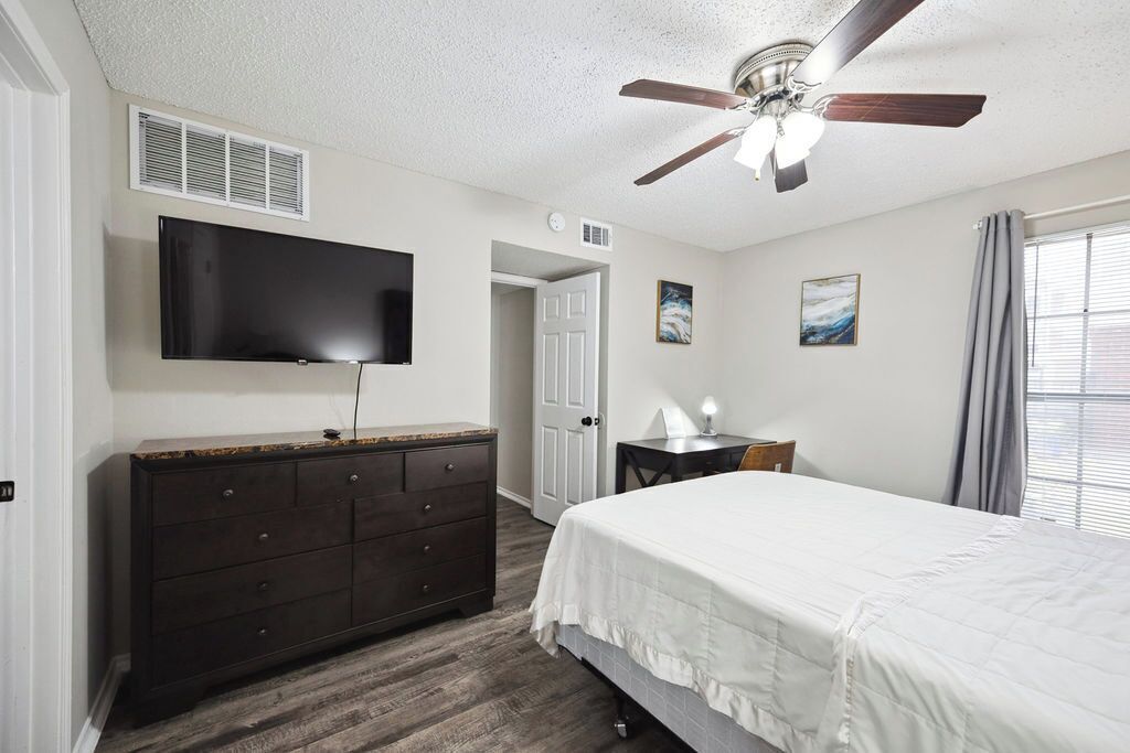 Ein Schlafzimmer mit Bett, Kommode, Deckenventilator, Fernseher und Kunstwerken.