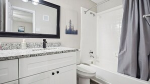 A bathroom with a white vanity, a sink, a mirror, a toilet, and a bathtub with a shower curtain.