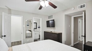 A bedroom with a large bed, a ceiling fan, a TV, and a dresser.