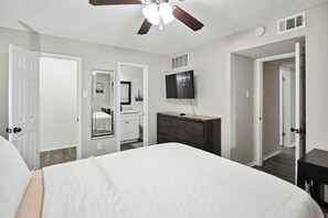 A bedroom with a large bed, a ceiling fan, a TV, and a dresser.