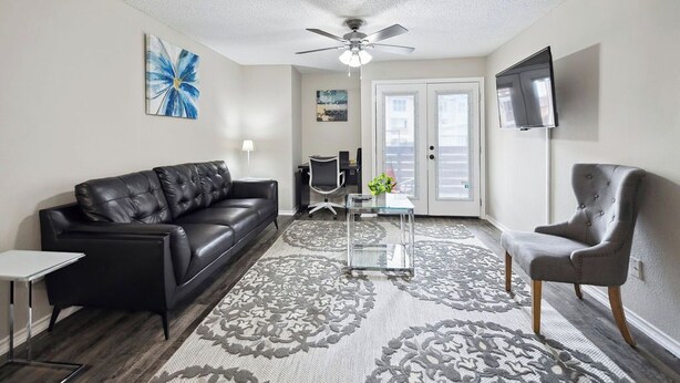 A living room with a black leather sofa, a grey armchair, a glass coffee table, and a patterned rug.