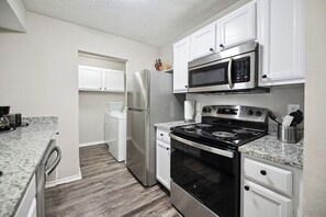 A modern kitchen with white cabinets, stainless steel appliances, granite countertops, and a wood floor.