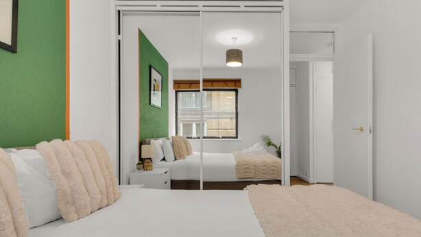 Une chambre à coucher avec un grand lit, une table de chevet, une commode et une fenêtre avec des stores.