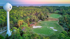 A golf course with a water tower, surrounded by dense forest.