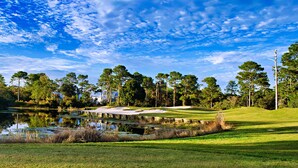 A golf course with a pond, sand bunkers, and tall trees.