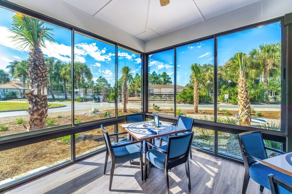 A sunlit room with large windows, a round table, and blue chairs.