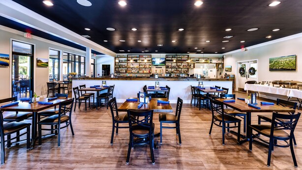 A restaurant with multiple tables and chairs, a bar area, and a view of the outdoors.