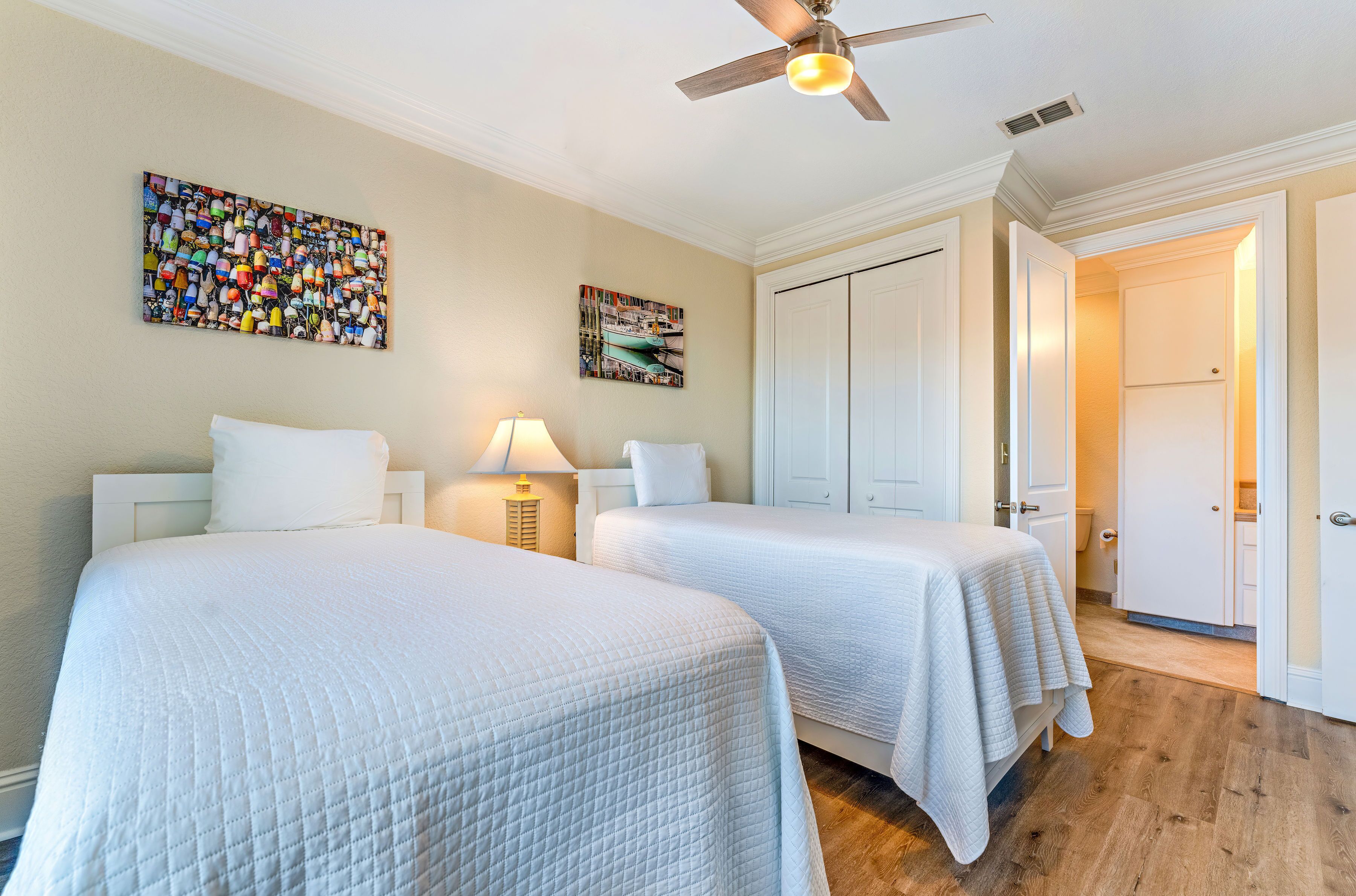 A hotel room with two beds, a ceiling fan, a wall-mounted artwork, and a door leading to a bathroom.