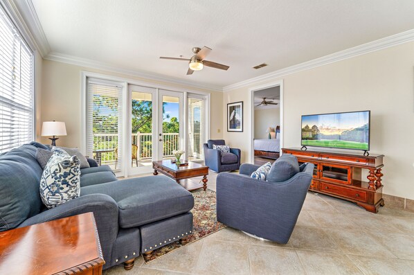 A living room with a sofa, armchair, TV, and ceiling fan.