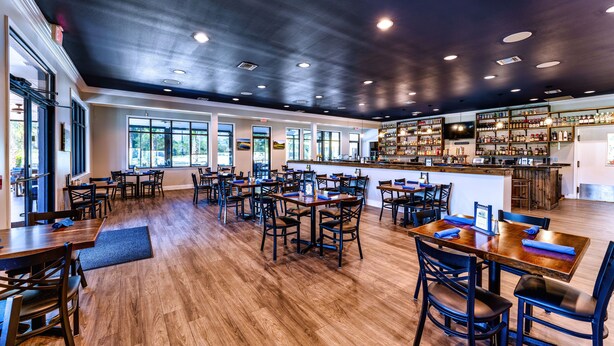 Un restaurant spacieux avec des tables et des chaises en bois, un coin bar et de grandes fenêtres qui laissent entrer la lumière naturelle.