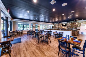 A spacious restaurant with wooden tables and chairs, a bar area, and large windows allowing natural light. - Final Putt Palace (Carrabelle)