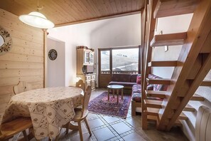 A cozy room with a wooden table, chairs, a sofa, and a view through a large window.