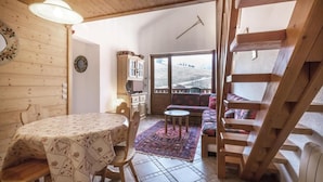 Une pièce chaleureuse avec une table et des chaises en bois, un canapé, un petit tapis et une vue par la fenêtre.