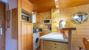 Une cuisine compacte dotée de meubles en bois, d’un four à micro-ondes, d’une machine à café et d’un lave-linge.