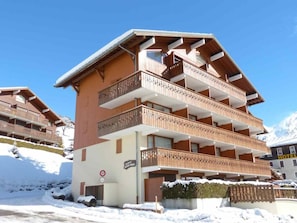 A multi-story hotel with balconies, a ski slope in the background, and a sign indicating a ski lift area.