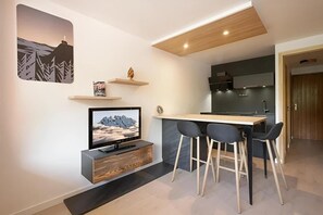 A modern living space with a flat-screen TV, a wooden coffee table, and bar stools.