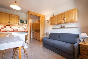 A compact kitchen with wooden cabinets, a dining table, and a grey sofa.