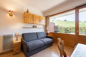 A room with a grey sofa, wooden cabinets, a window with a view of a green landscape, and a small wooden chair.
