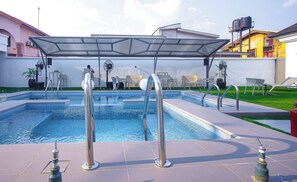 A swimming pool with a glass enclosure, lounge chairs, and a covered seating area.