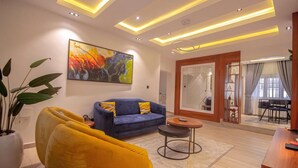 A modern living room with a blue sofa, yellow armchair, and a painting on the wall. - BnJ Benin City Oasis - Spacious 3BR Apartment (Benin City)
