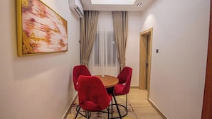 Un couloir étroit avec une table ronde en bois et quatre chaises rouges, un luminaire au plafond, un tableau accroché au mur et une porte au fond.