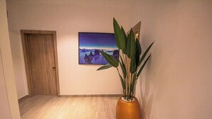 Un couloir avec une porte en bois, un tableau encadré au mur et une plante en pot.