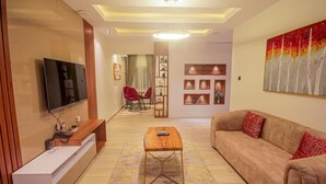Un salon moderne avec un téléviseur à écran plat, une table basse en bois, un canapé beige agrémenté de coussins rouges et un fauteuil rouge.