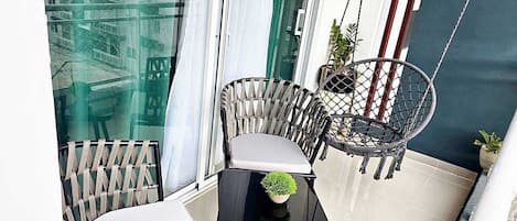 En balkon med to fletstole, et lille bord og en potteplante.