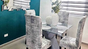 Un coin repas avec une table en verre, des chaises à motifs, un lustre moderne et un mur d’accent bleu.