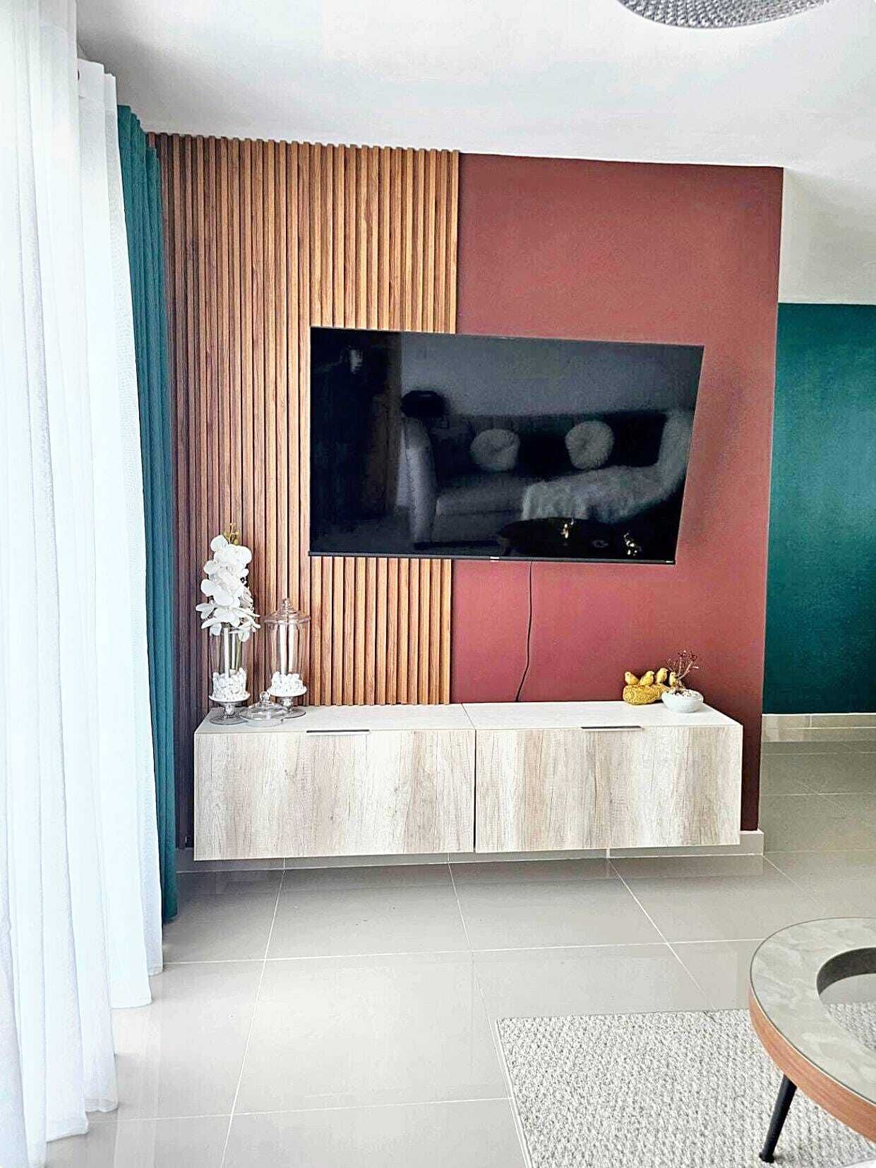 Een moderne woonkamer met een flatscreen televisie bevestigd aan een wand met houten paneel en een rode accentwand. Er staat een witte console met decoratieve objecten en een kleine plant.