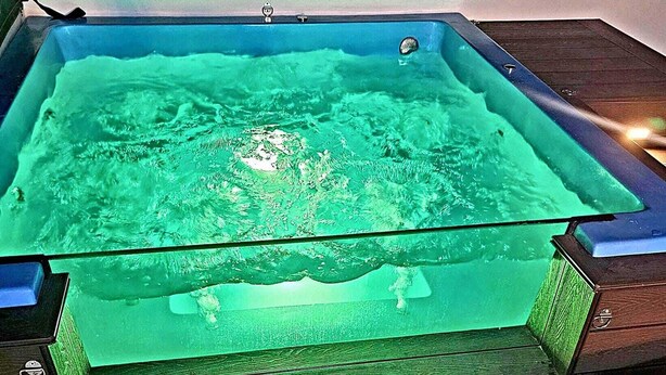 Un bain à remous rectangulaire avec un dessus en verre, doté d’une base verte, installé sur une terrasse en bois.