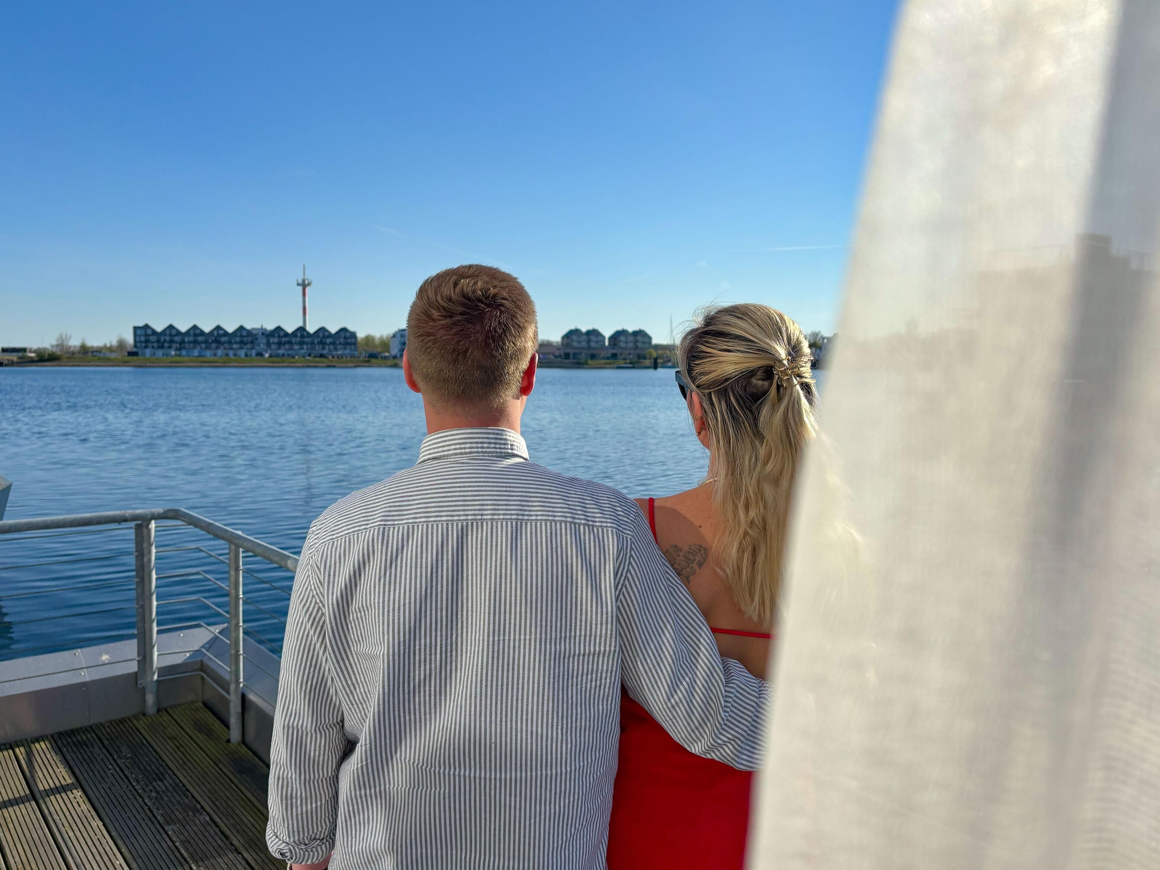 A couple on a boat deck overlooking a body of water with buildings in the background.