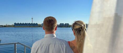 A couple on a boat deck overlooking a body of water with buildings in the background.