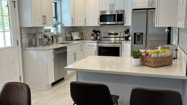 A modern kitchen with white cabinets, stainless steel appliances, and a central island with bar stools. - Gorgeous Florida Pool and Spa Home (Jacksonville)