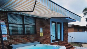 A hot tub in a backyard with a striped awning, brick walls, and a white fence. - Gorgeous Florida Pool and Spa Home (Jacksonville)