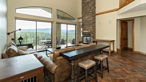 A spacious living area with a large stone fireplace, a dining table with bar stools, and a view of the mountains through large windows.