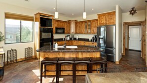 A modern kitchen with wooden cabinets, stainless steel appliances, a large island with bar stools, and pendant lighting.