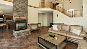 A spacious living area with a stone fireplace, leather sofa, and a wooden staircase.