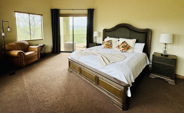 A bedroom with a large bed, a leather chair, a nightstand, and a view of the outdoors.