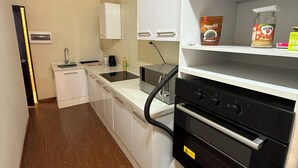 Eine moderne Küche mit weißen Schränken, einem Einbauofen und einer Mikrowelle. Auf der Arbeitsplatte befindet sich ein Regal mit Küchenutensilien sowie eine Kaffeemaschine.