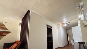 Ein Flur mit Treppe, Deckenventilator und Küchenbereich mit Kühlschrank und Hocker.
