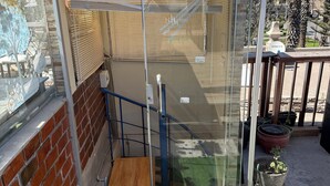 Ein gläserner Balkon mit einer Holztreppe, einer Ziegelwand und Topfpflanzen.