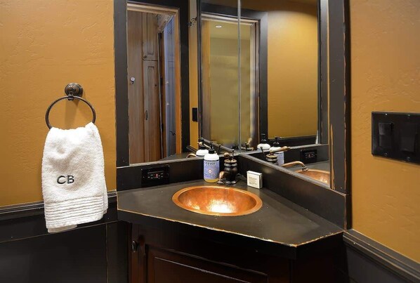 A bathroom with a copper sink, a towel rack with a white towel, a mirror, and a door. - Silver Ridge 6 (Crested Butte)