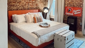 Een slaapkamer met een bakstenen muur, houten plafond, een bed met wit beddengoed, een hangende lamp en een geïnstalleerde airconditioning.