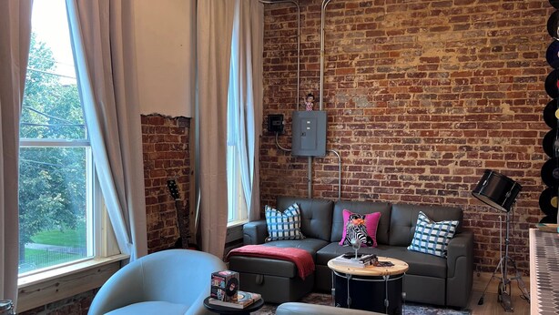 Een moderne woonkamer met een bakstenen muur, een grijze bank, een ronde salontafel en een ruime fauteuil.