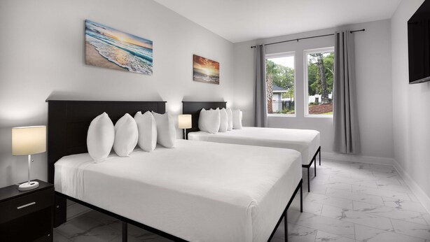 A hotel room with two beds, a nightstand with a lamp, and artwork on the walls. - Ocean Escape Condos North (North Myrtle Beach)